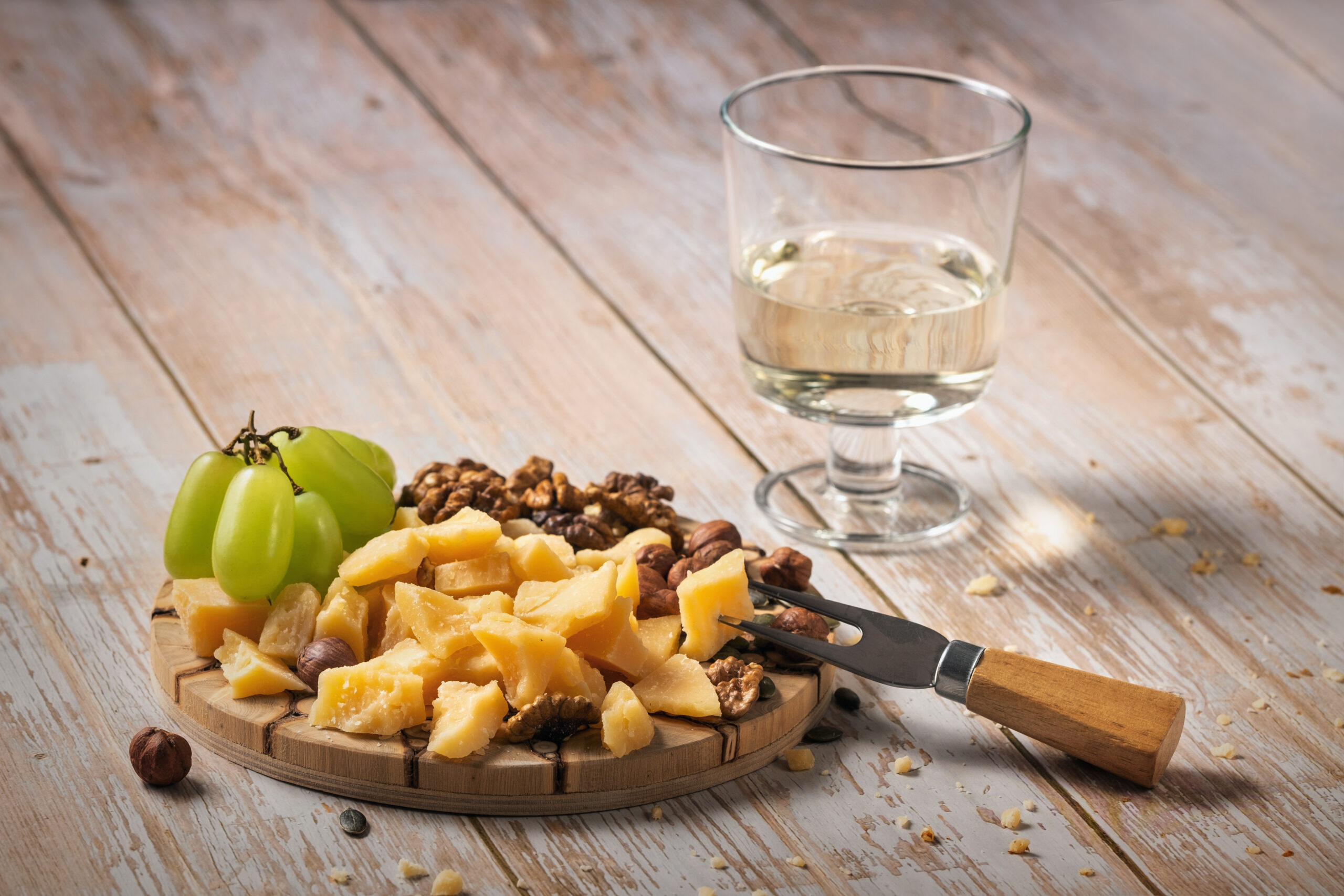 Cheese plate with a variety of snacks on a wooden table with a glass of wine.